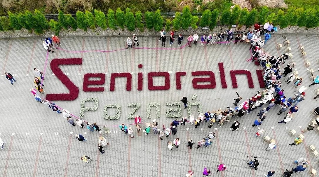 An overhead view of people gathered to form the shape of a heart around the words "Senioralni Poznań" spelled out in flower beds.